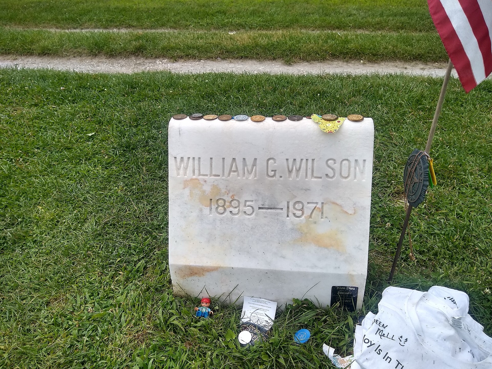 A plain granite gravestone reading William G. Wilson 1895 to 1971, with sobriety chips and coins lined up along the top edge.