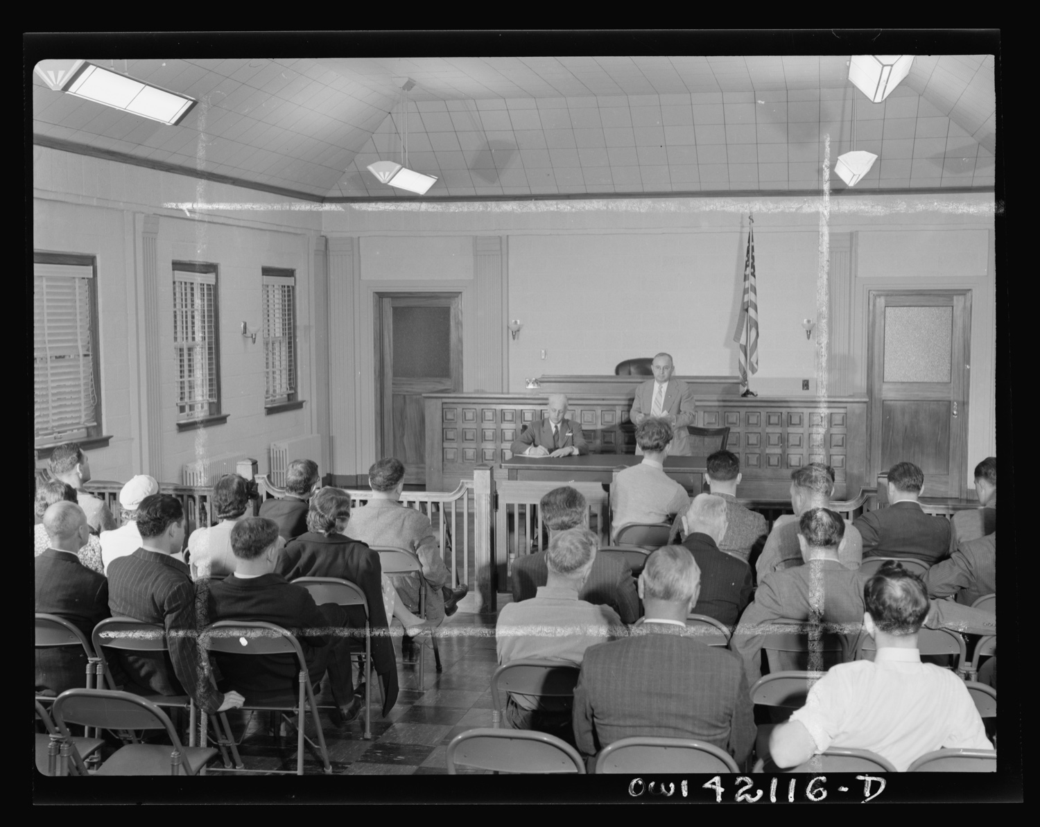 Rows of men in suits sitting on folding chairs in a plain New England hall, seen from behind.