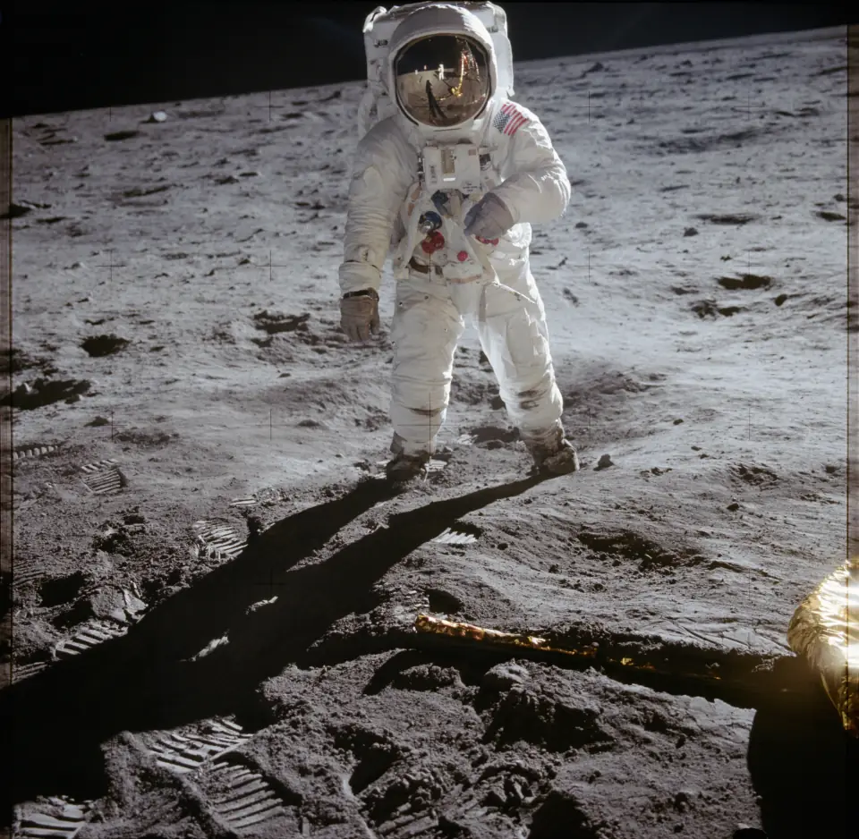 Buzz Aldrin standing on the Moon, Neil Armstrong and the lunar module reflected in his gold visor.