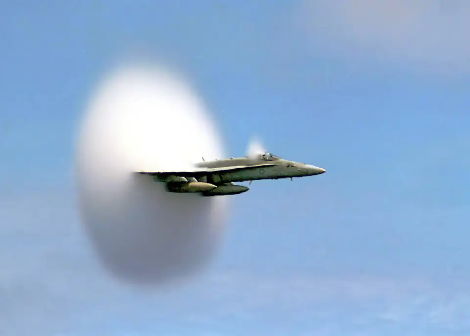 An F/A-18 Hornet skimming low over the ocean, wrapped in a perfect white cone of condensation at the edge of the sound barrier.