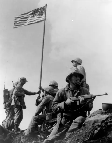 Marines around the first, smaller flag raised on Mount Suribachi a few hours earlier.