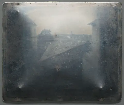 The actual Niepce pewter plate photographed in raking light in 2020: a shiny gray metal rectangle with the faint image barely visible.
