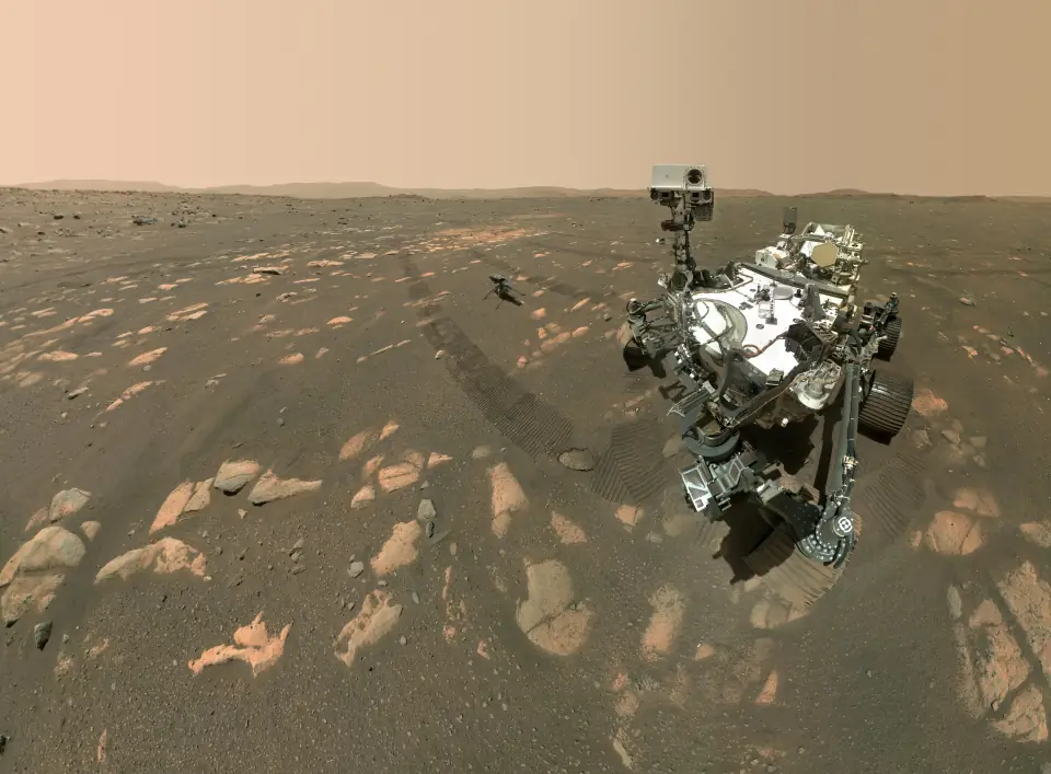 The Perseverance rover's selfie on Mars: the rover looking at the camera on rocky orange ground, with the small Ingenuity helicopter sitting a few meters behind it.