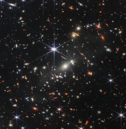 Webb's First Deep Field: a dense cluster of galaxies with gravitationally lensed arcs of light bent around it.