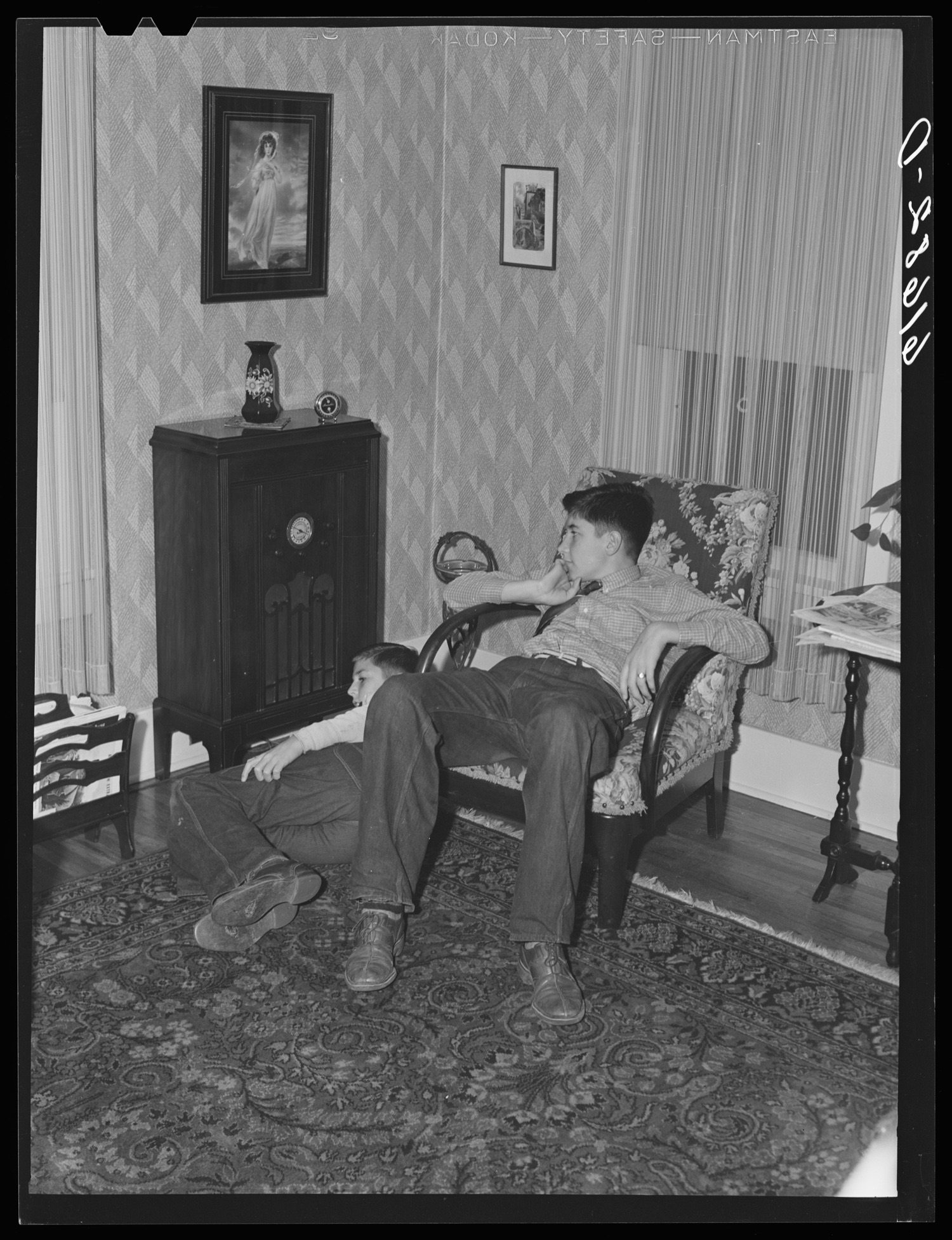 Two farm boys slumped beside a tall console radio in a 1940 living room.