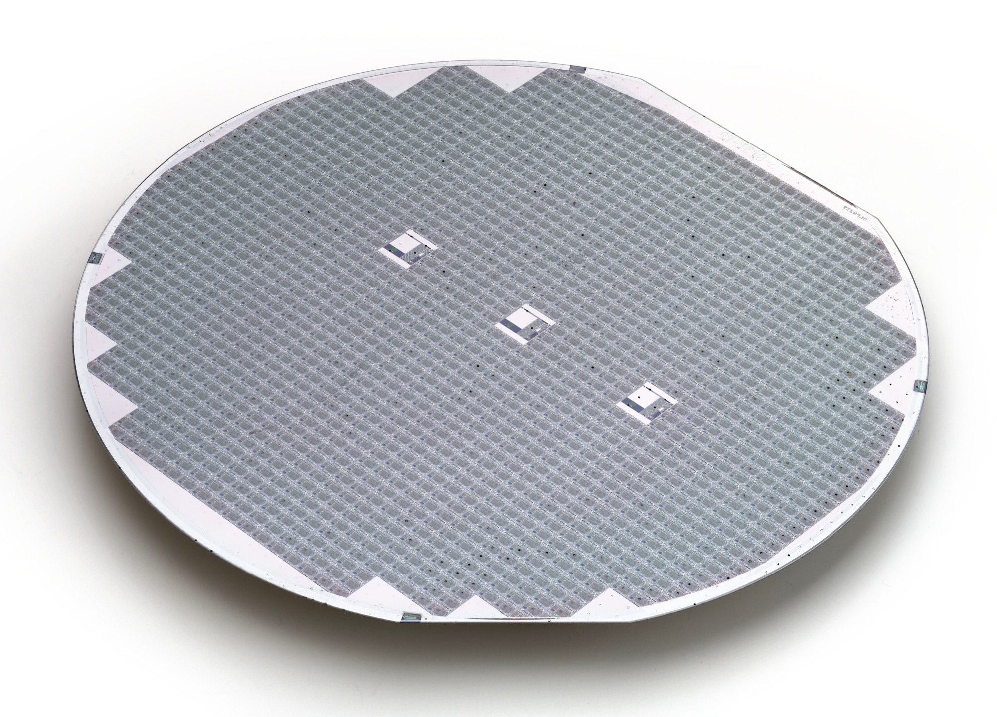 A finished silicon wafer covered edge to edge in a fine grid of identical chips, divided by the narrow saw streets along which it will be cut apart.