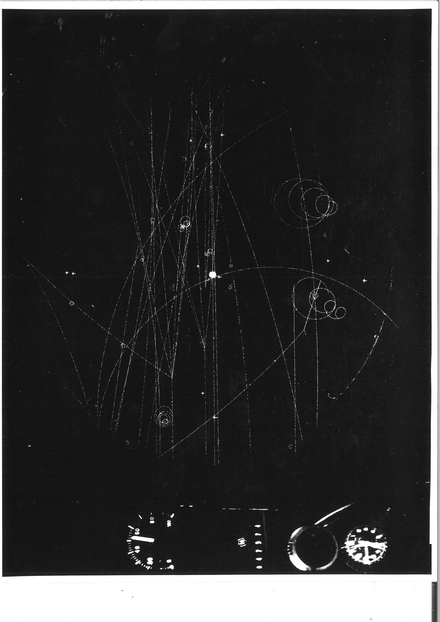 A bubble chamber photograph showing curling and spiraling white tracks left by subatomic particles moving through liquid in a magnetic field.