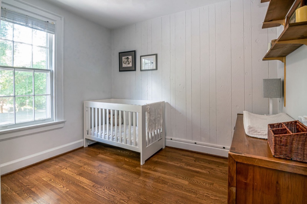 An empty crib with only a fitted sheet on a bare mattress, in a calm, sunlit room.