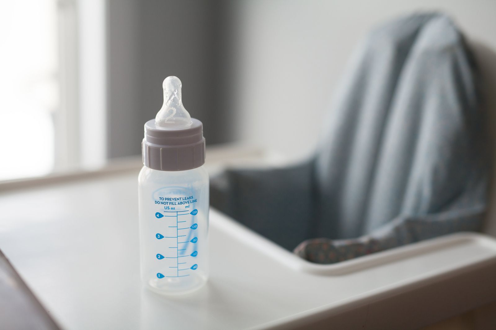 A clean, empty baby bottle with measurement markings on a white surface in soft natural light.