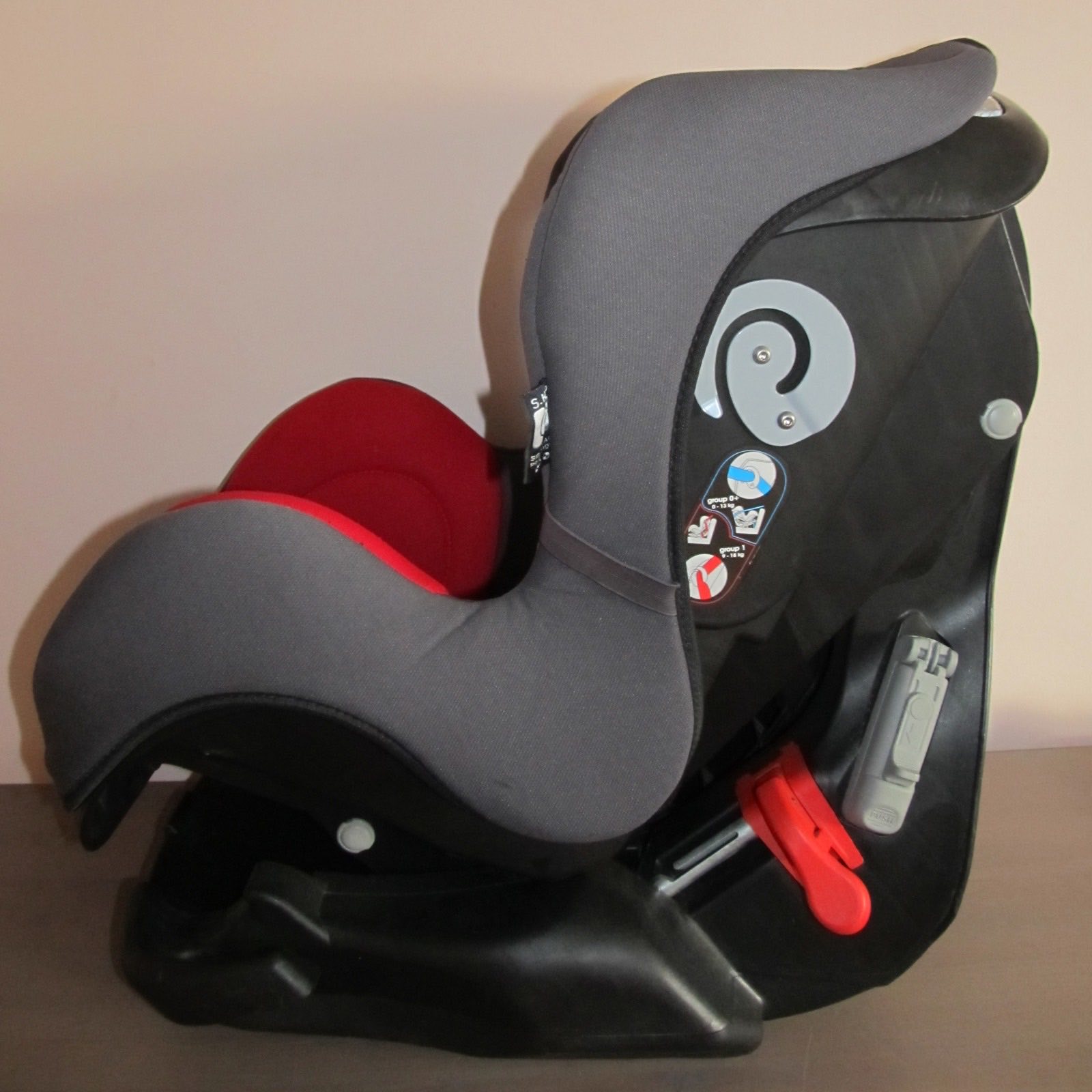 A rear-facing infant car seat shown in profile, reclined, with the harness and group label visible.