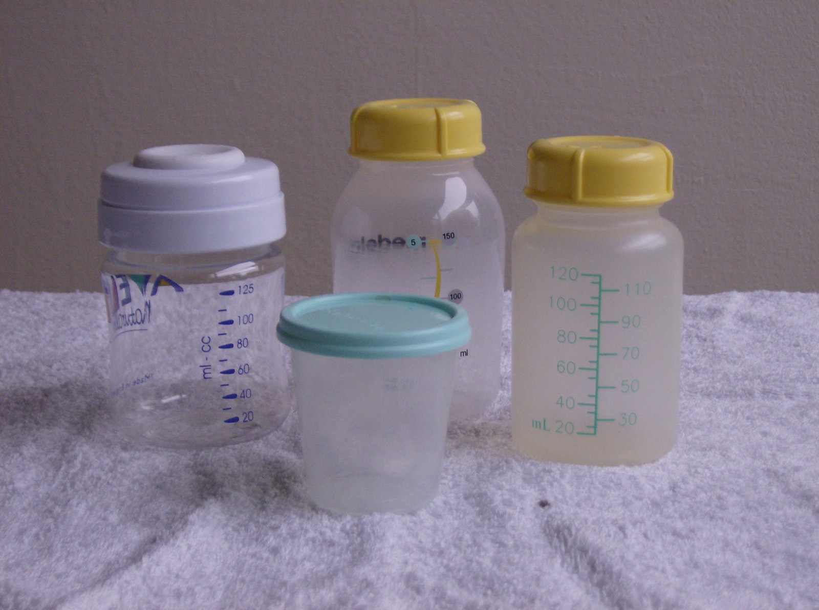 Bottles and cups of expressed breast milk arranged on a cloth.