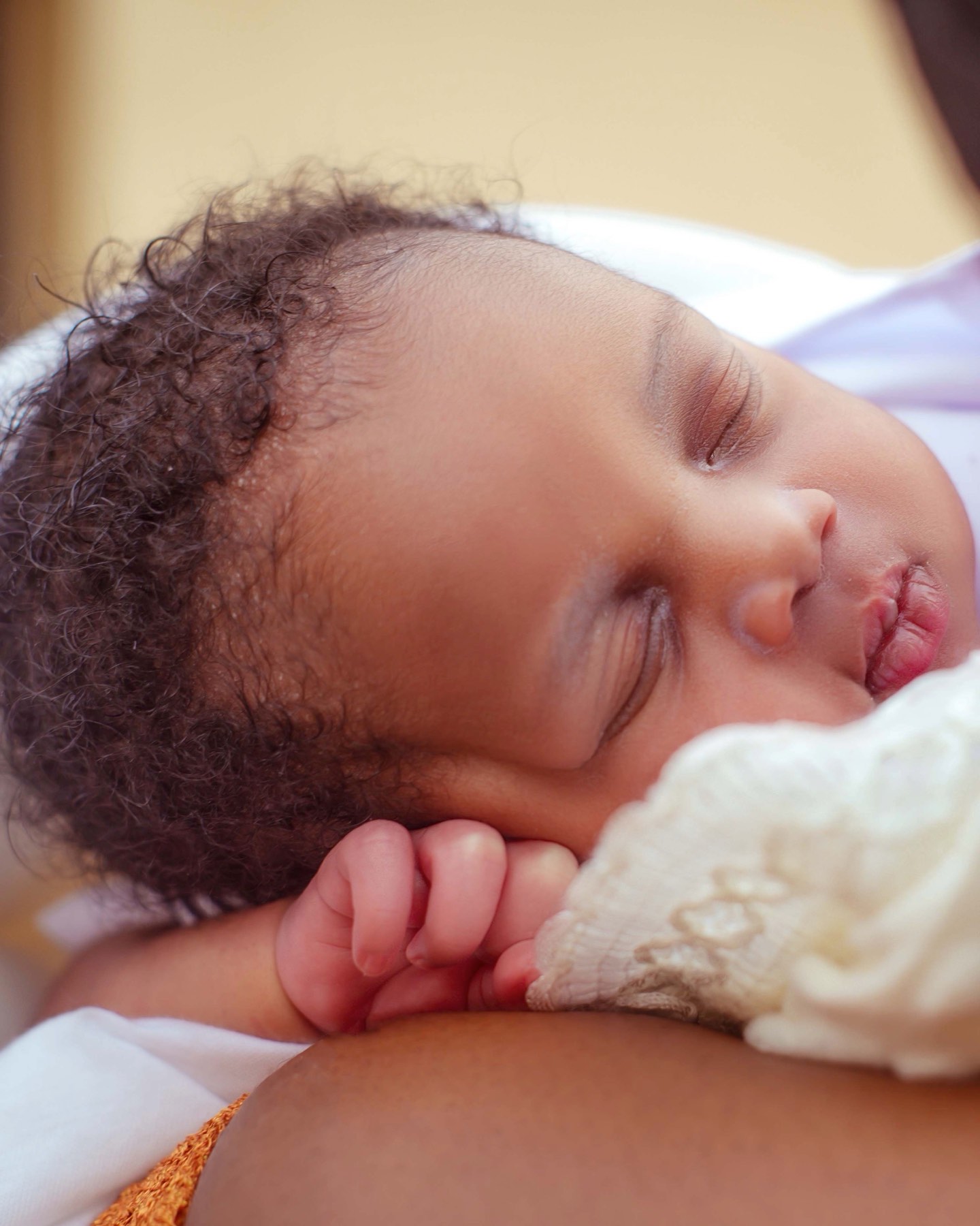 A peaceful sleeping newborn resting against a parent's shoulder in soft, warm light.