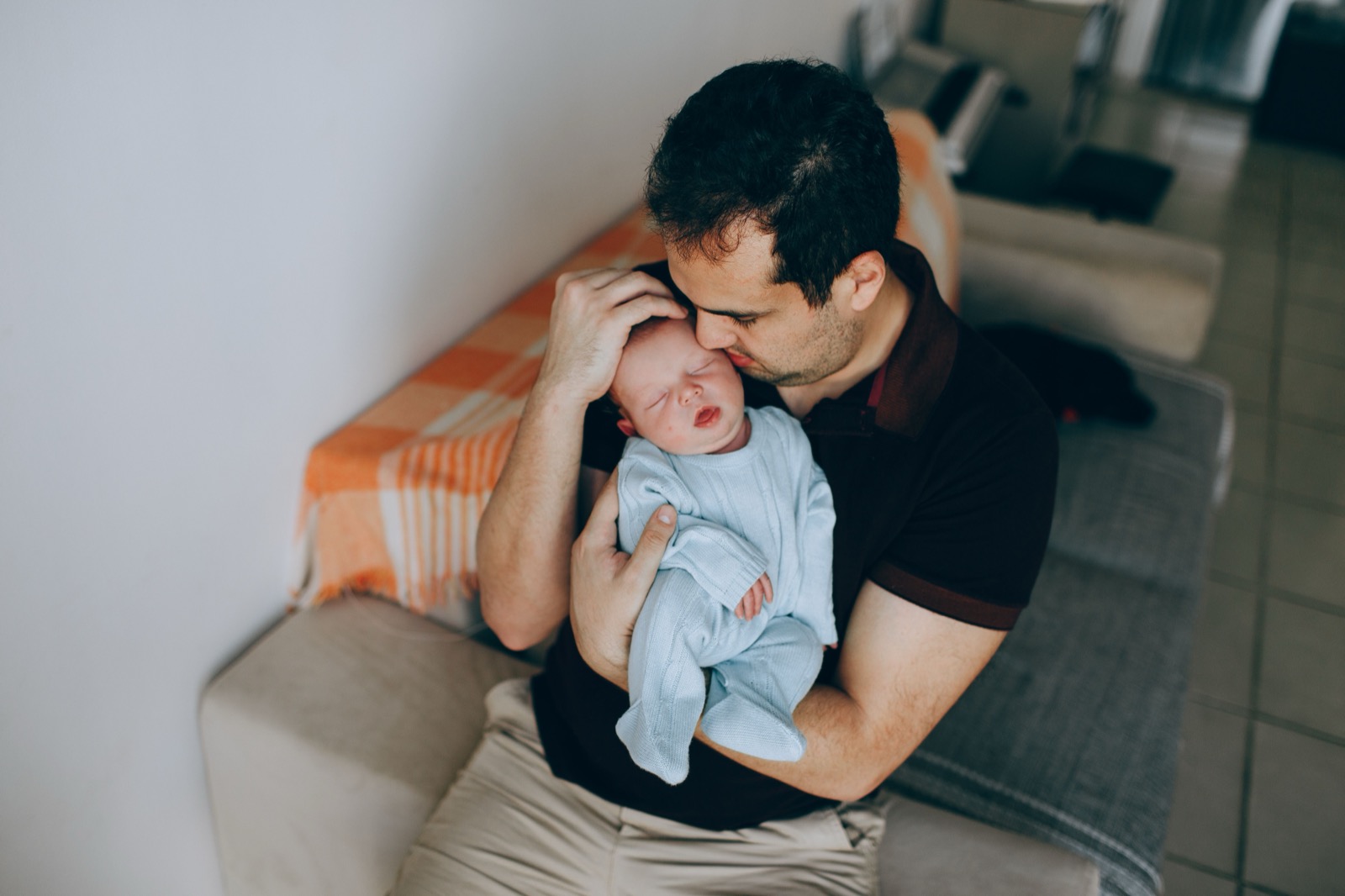 A parent sitting on a couch cradling a sleeping newborn.