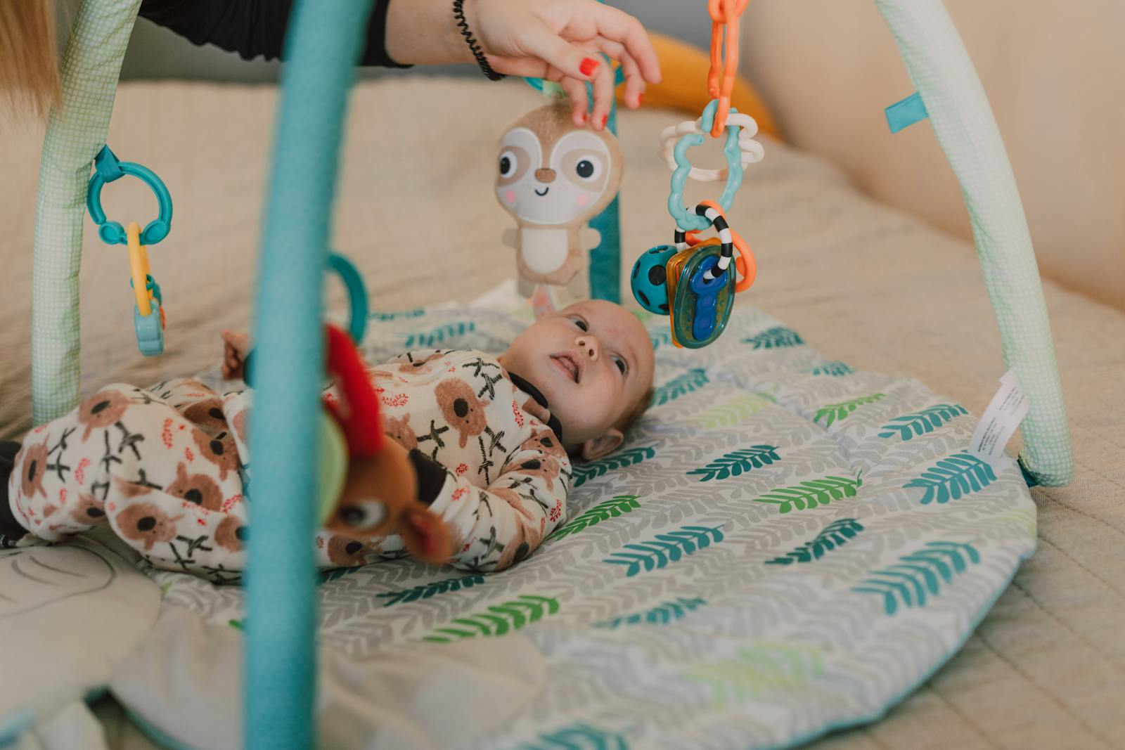 A baby on a padded play mat reaching toward soft toys hanging from an arch.