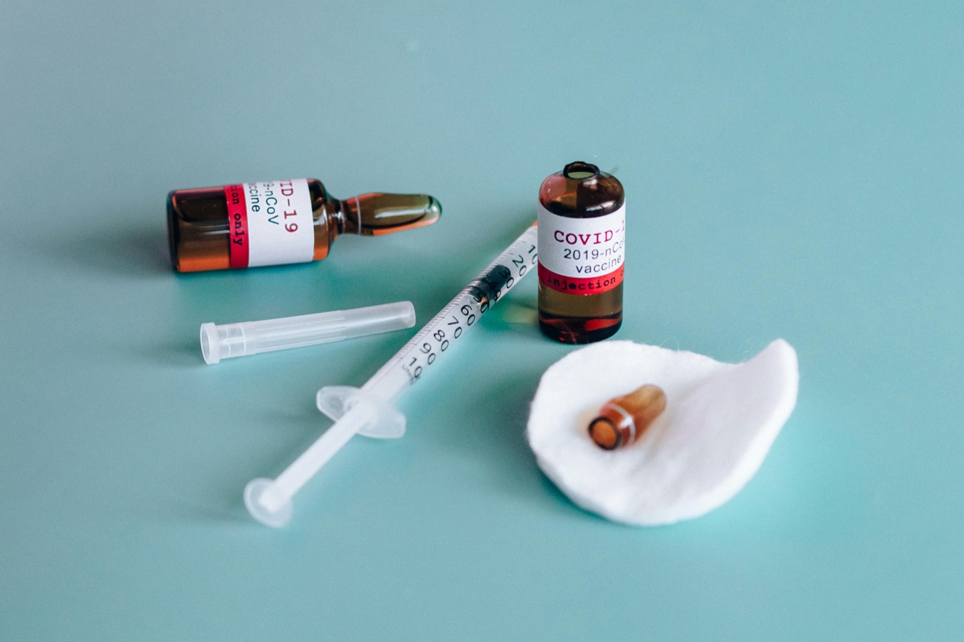 Two vaccine vials beside a syringe and a cotton pad.