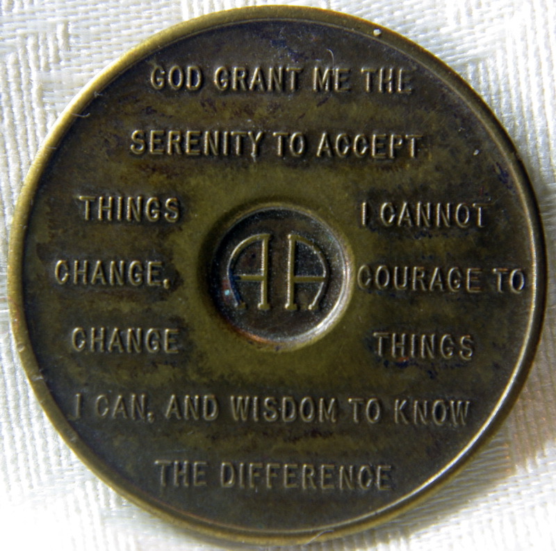 A bronze sobriety medallion photographed close up, the full Serenity Prayer engraved on its reverse.