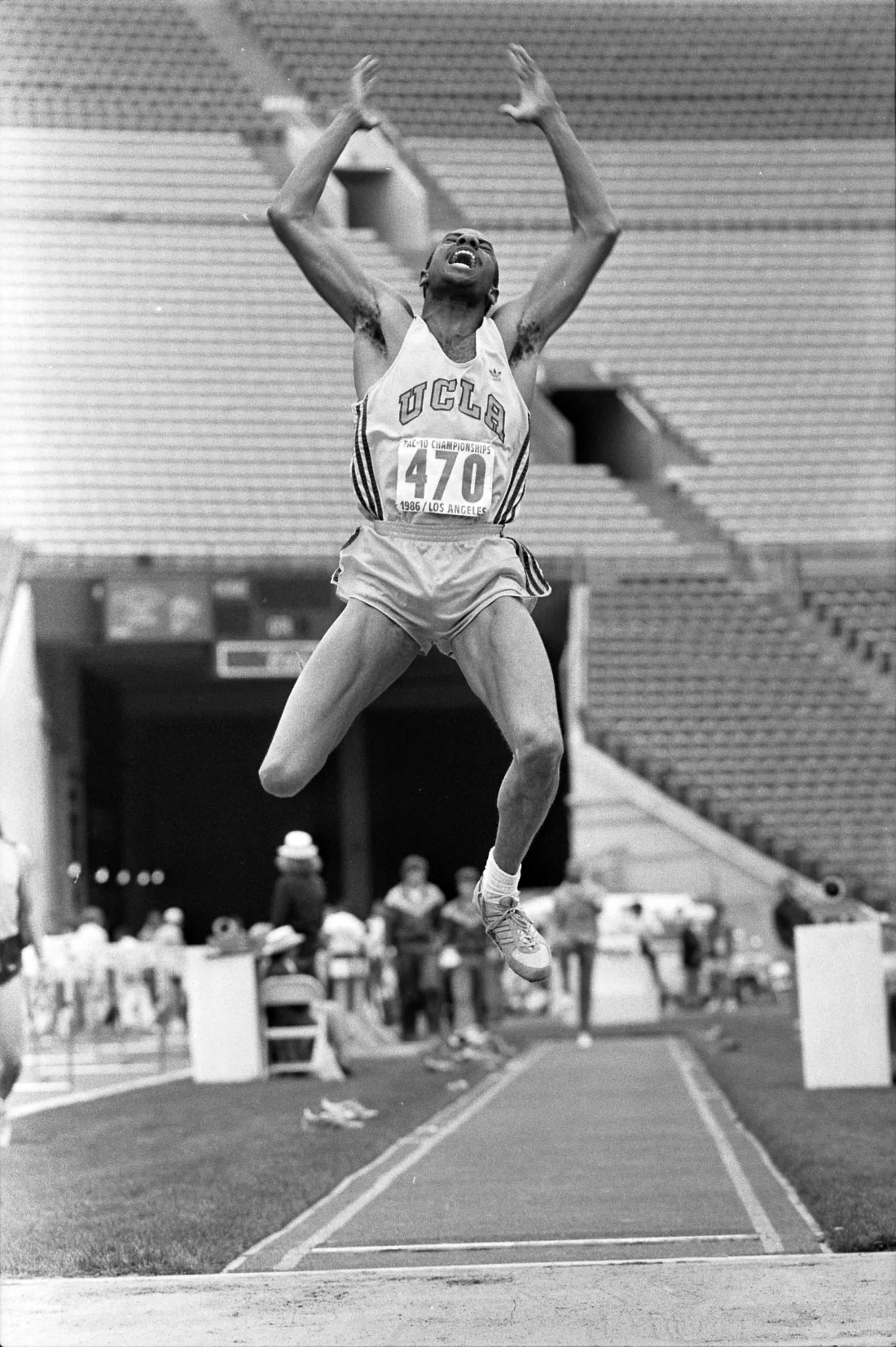 Long jumper Mike Powell stretched out at full extension in mid-air over the sand pit, arms thrown overhead, in a near-empty stadium.