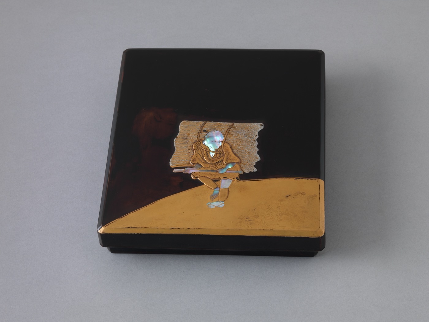 A black lacquer writing box with a woodcutter and trees rendered in gold, against a dark ground.