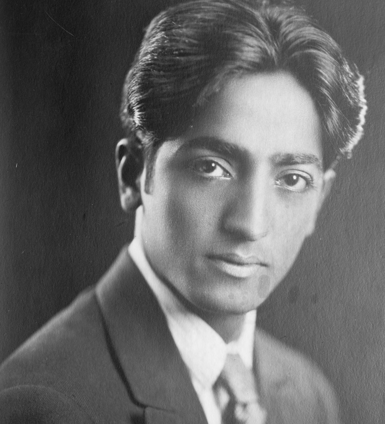 Jiddu Krishnamurti as a young man, a 1920s studio portrait: dark wavy hair, a quiet steady gaze, suit and tie.