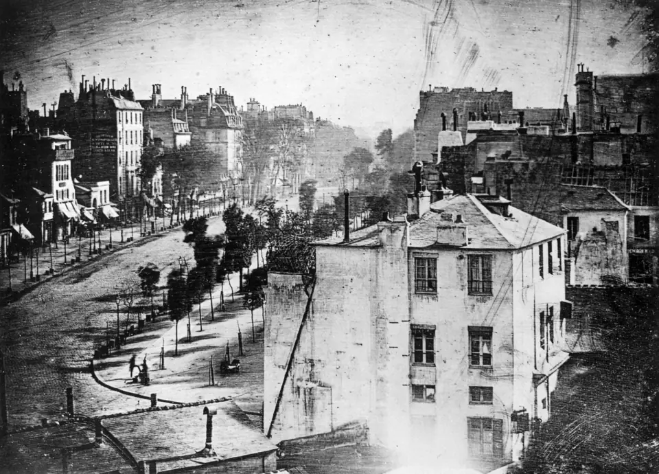 Boulevard du Temple, Paris, 1838: a long daguerreotype view of an empty-looking boulevard, with one tiny man standing at a shoeshine stand in the lower left.