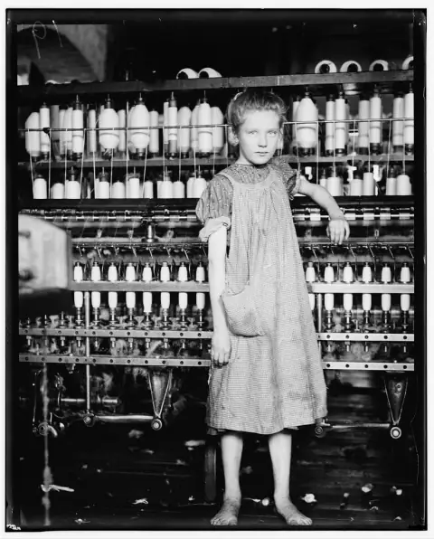 Addie Card, a barefoot twelve-year-old spinner, leaning on a spinning frame in a Vermont cotton mill, 1910.