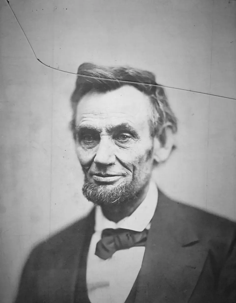The cracked-plate portrait of Abraham Lincoln, 1865: a close, tired, faintly smiling Lincoln with a crack in the negative arcing across the top of the image.