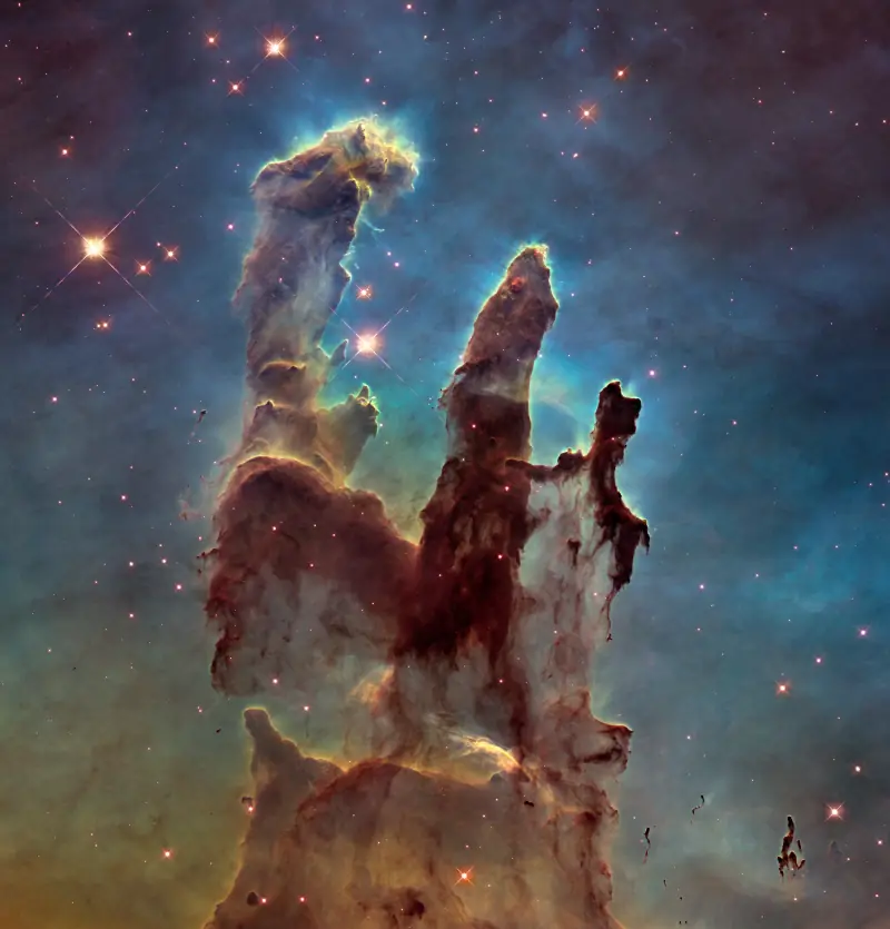 The Pillars of Creation seen by the James Webb Space Telescope: sharp rust-red columns of gas crowded with stars.
