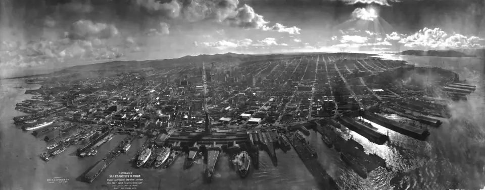 San Francisco in Ruins, May 1906: a sweeping aerial panorama of the burned city from two thousand feet over the bay, sun glinting on the water.