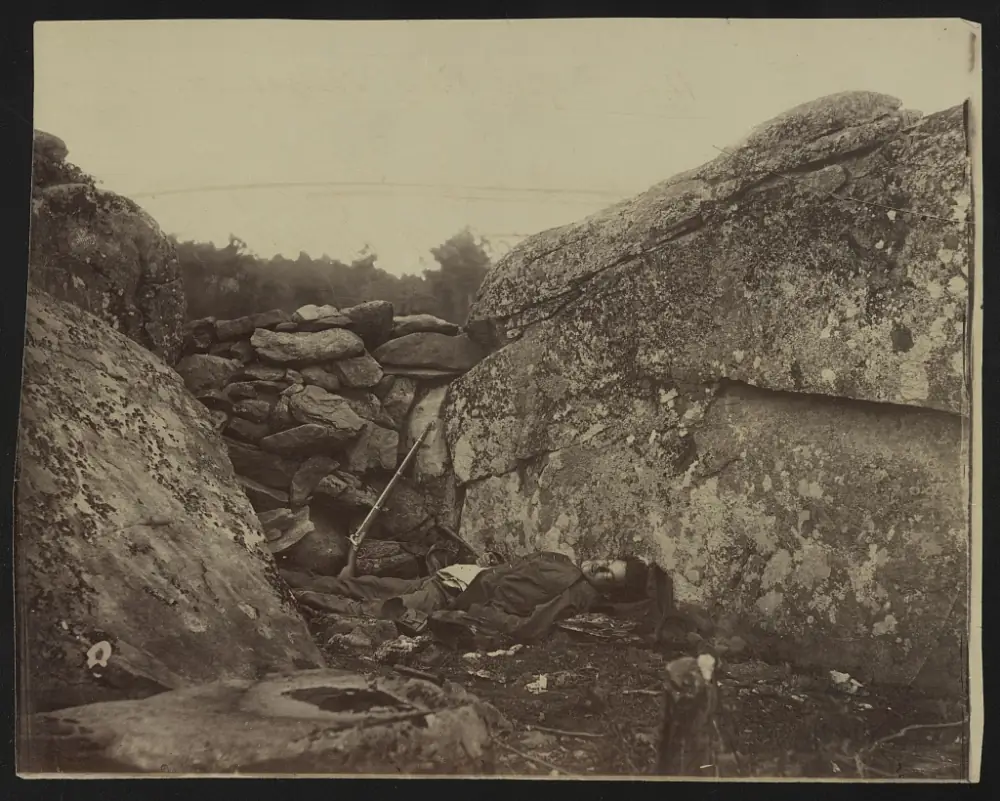 Home of a Rebel Sharpshooter, Gettysburg 1863: a dead Confederate soldier lying in a stone-walled rocky den, a rifle propped against the wall.