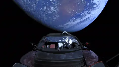 Starman: a spacesuited mannequin at the wheel of a red Tesla Roadster in space, Earth glowing behind the open car.