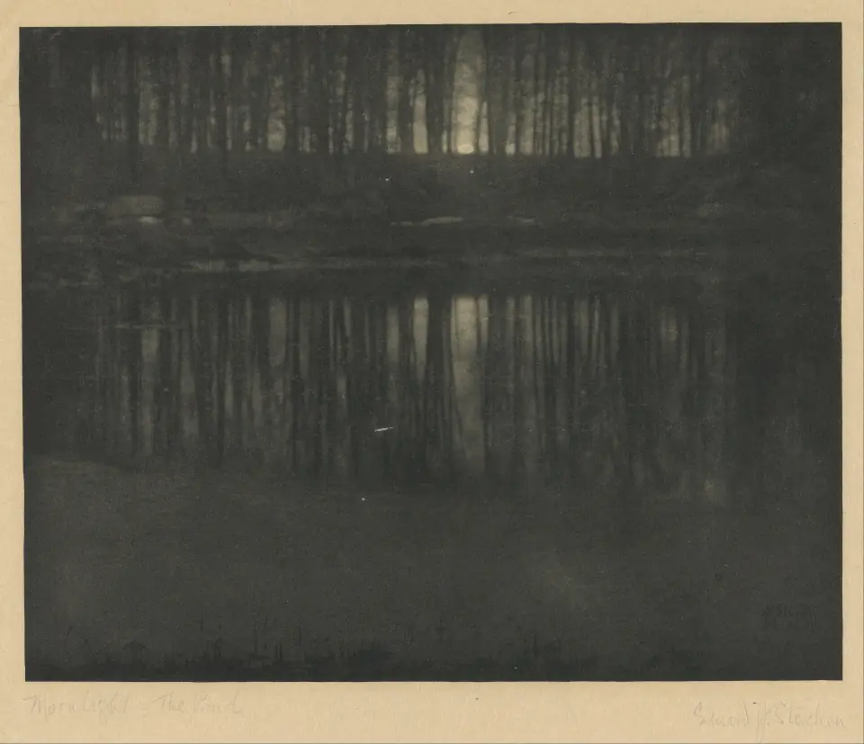 The Pond, Moonlight, 1904: a dark dreamlike pond between trees with a moonglow breaking through, in hand-applied blue-green tones.
