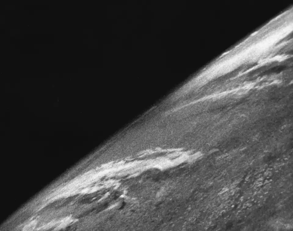 The first photograph from space, 1946: a grainy black-and-white curve of Earth under the black of space.