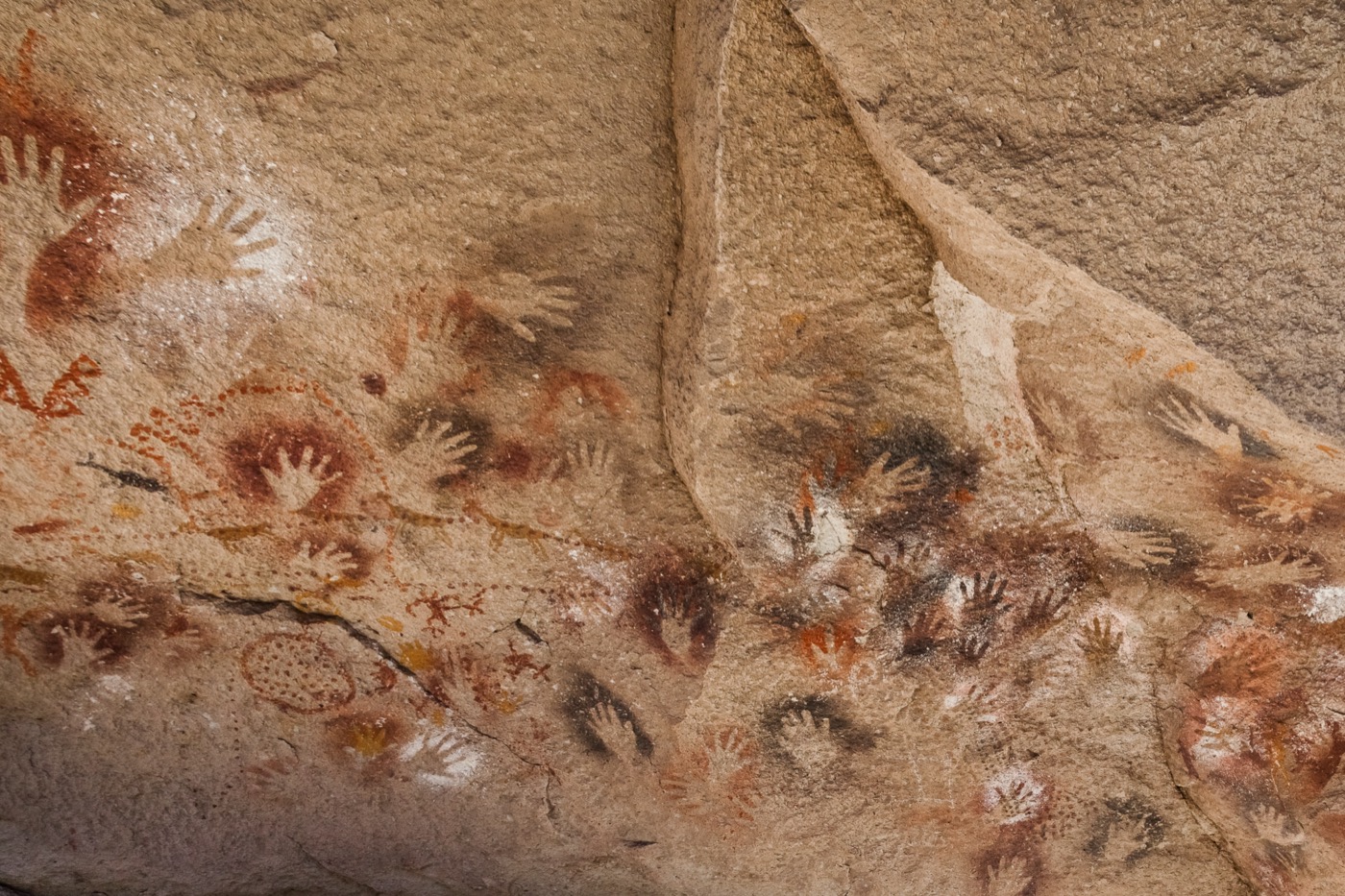 Dozens of human handprints stencilled in red, ochre, and white across a sandstone cave wall.