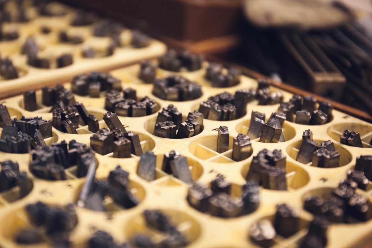 A tray of metal letterpress type, the cast sorts clustered in the round wells of a warm cream type case under soft light.