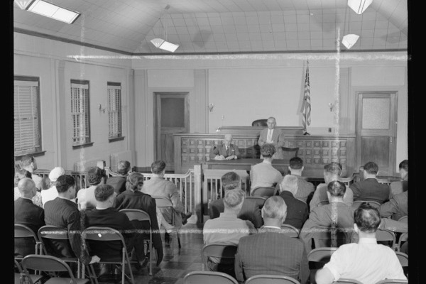 Rows of people seen from behind on folding chairs in a plain hall, an anonymous meeting room.