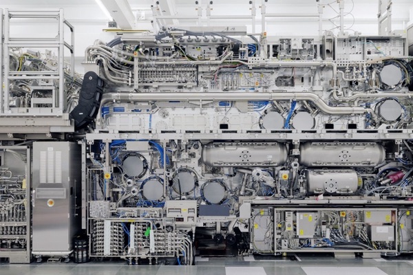 The ASML High-NA EUV lithography machine photographed head-on: an intricate wall of silver vacuum vessels, cabling, and modules in a white cleanroom.