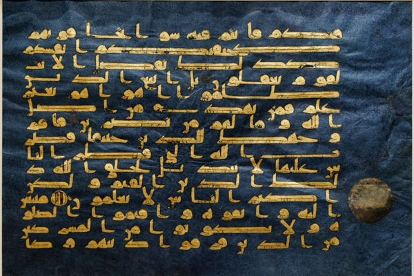 A page from the Blue Qur'an: rows of angular gold Kufic Arabic script on deep indigo-dyed parchment, with a circular verse-marker at the right.