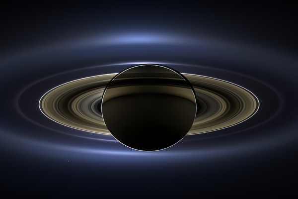 Saturn seen from its shadow, a dark globe rimmed with sunlight inside luminous gold and blue rings.